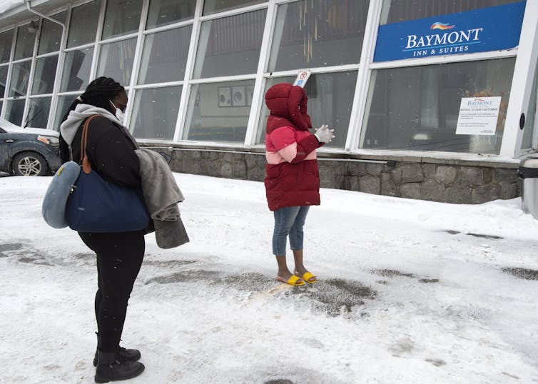 Two women wait in the snow outside a hotel